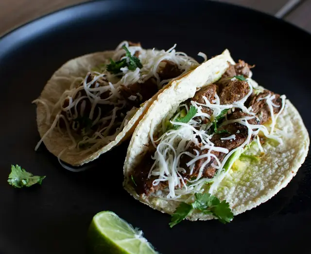 Two tacos with lime on a black plate
